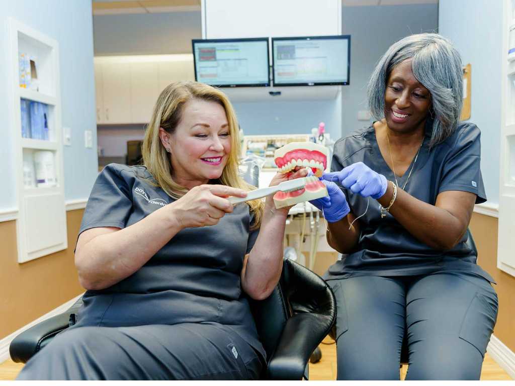 The Connection Between Oral Health and Overall Wellness 10 Two dental professionals demonstrate oral hygiene techniques using a large model of teeth in a modern dental office.