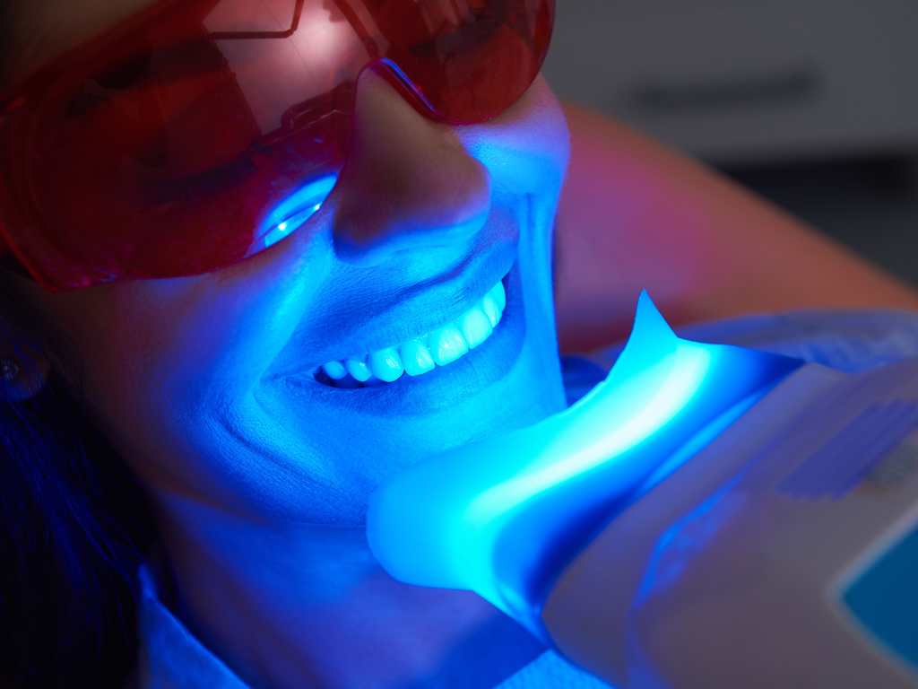 A blue LED light therapy device is positioned near a person's neck, indicating a skincare treatment in a clinical environment.